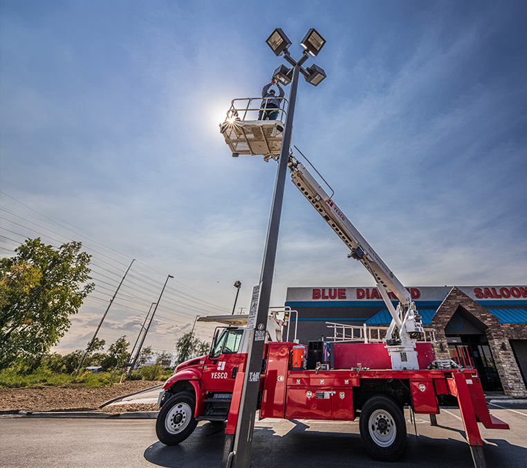 A worker stands on an elevated platform attached to a red utility vehicle