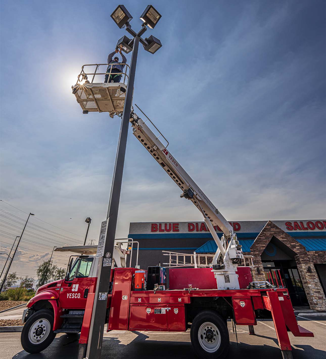 A worker stands in a raised bucket lift attached to a red YESCO truck