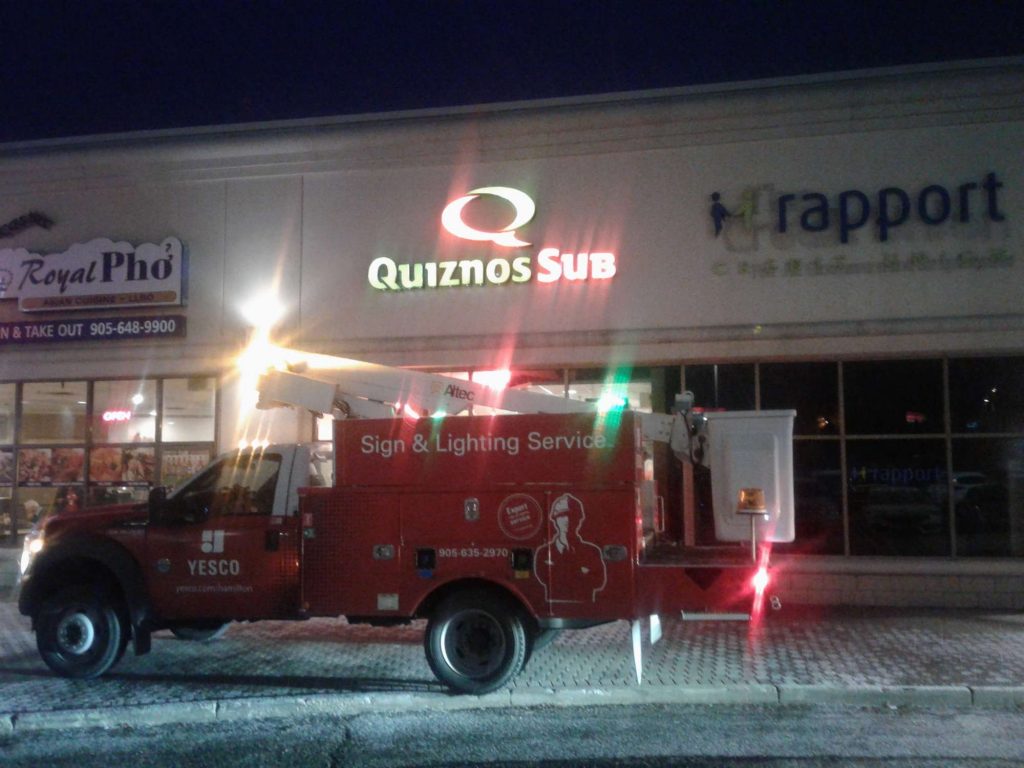 Quiznos Sub sign illuminated at night with the red Yesco truck in front of the building