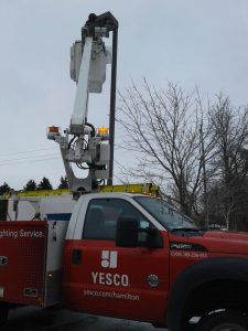 red Yesco service truck with the bucket ladder up fixing a pole light in a parking lot