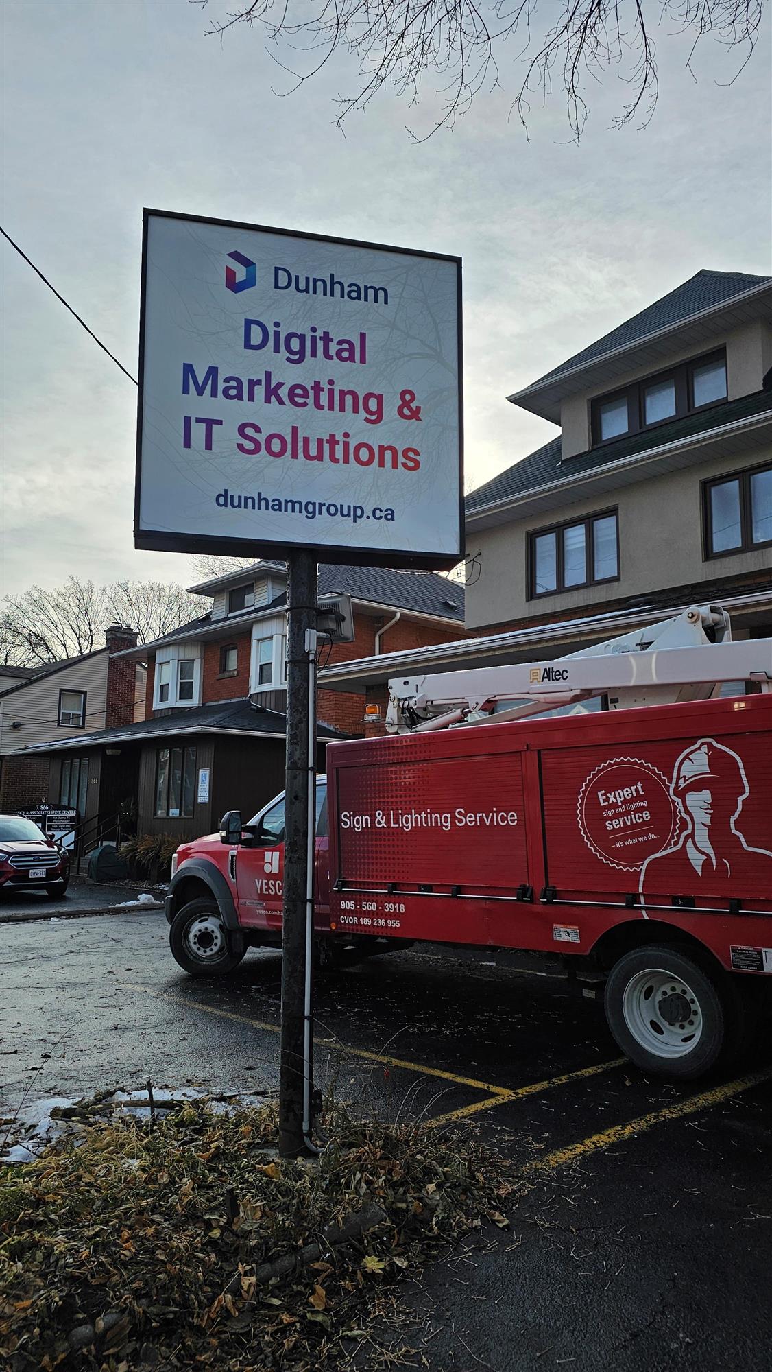 a red Yesco truck beside a newly installed pole sign for Dunham Digital Marketing & IT Solutions
