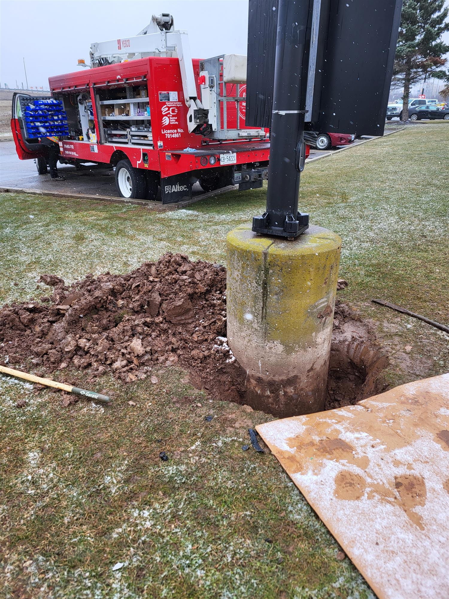 A red Yesco truck parked beside a cement base and pole to repair underground wiring