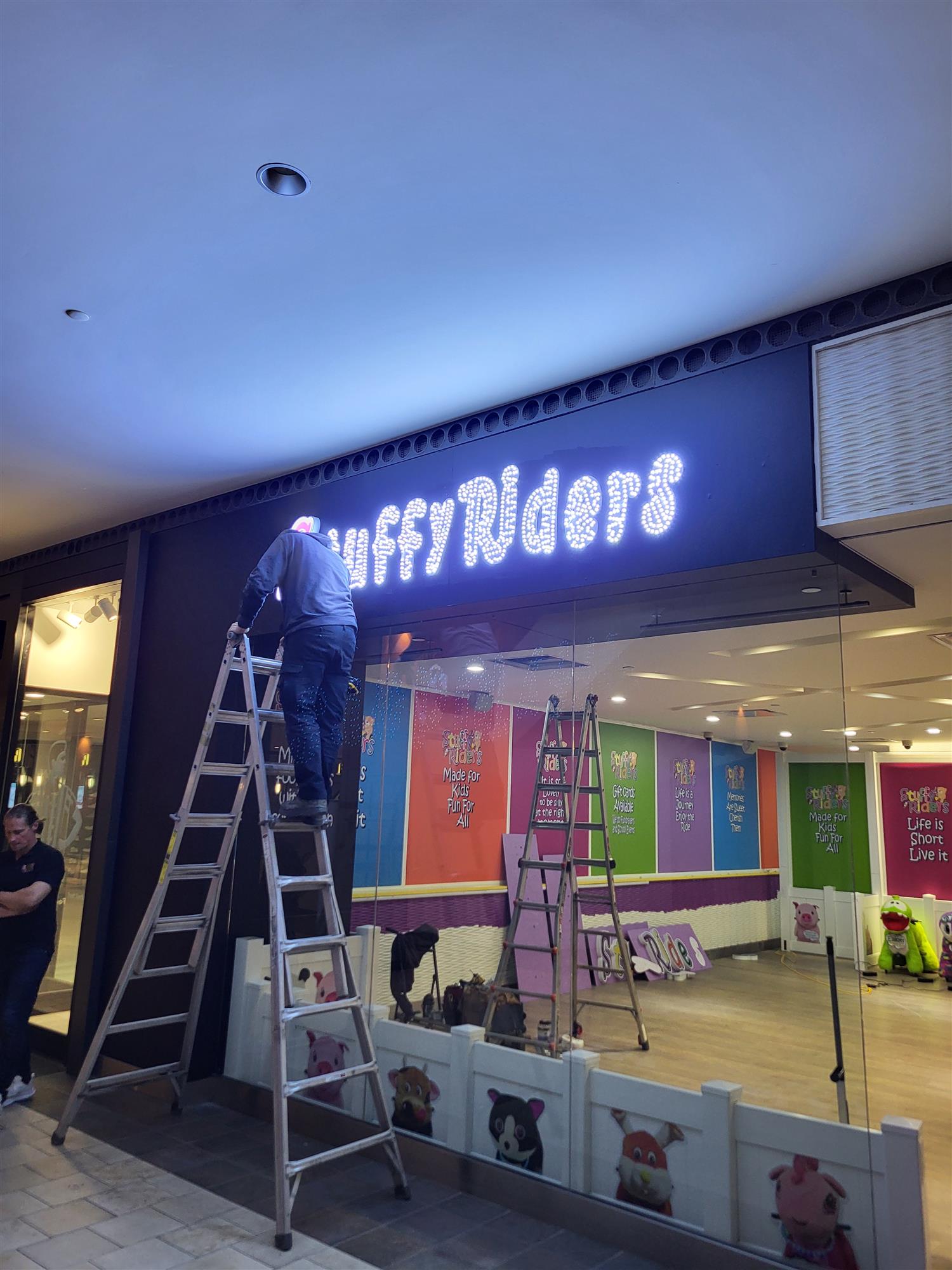 man on ladder in front of store with Stuffy Riders signs