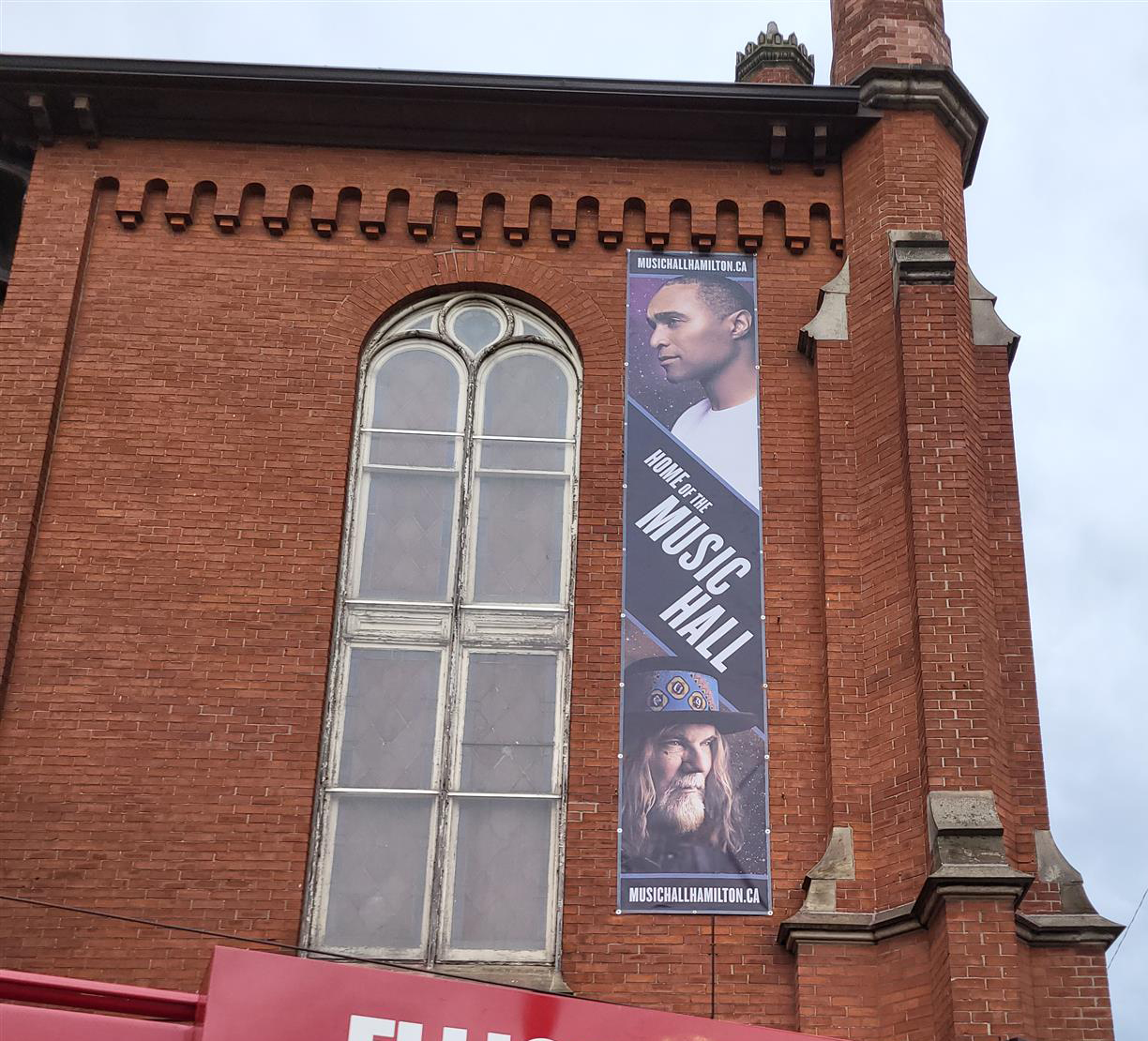 an old brick building with banner advertising Music Hall Hamilton with two men's faces