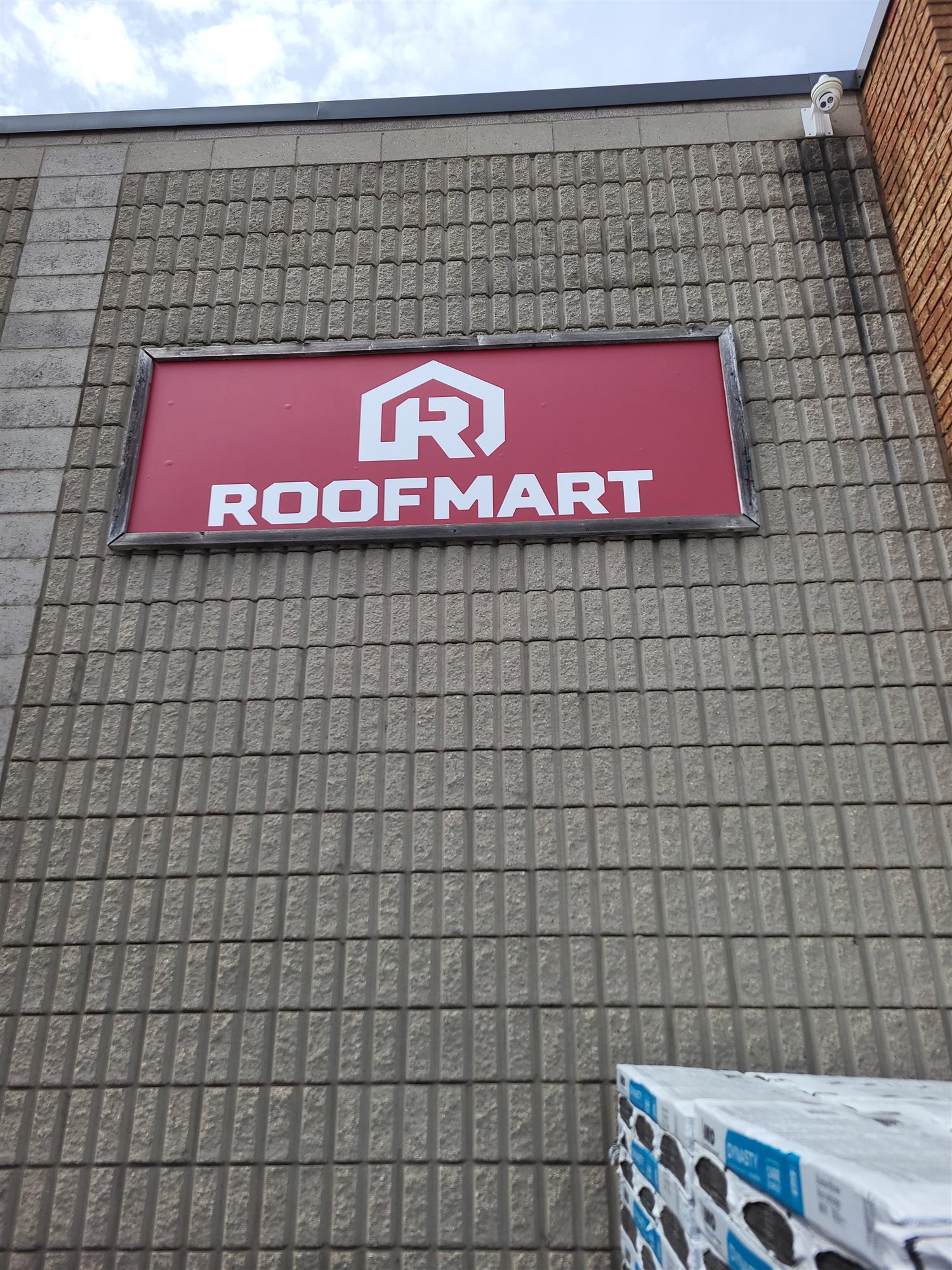 a red and white Roofmart sign on side of brick building