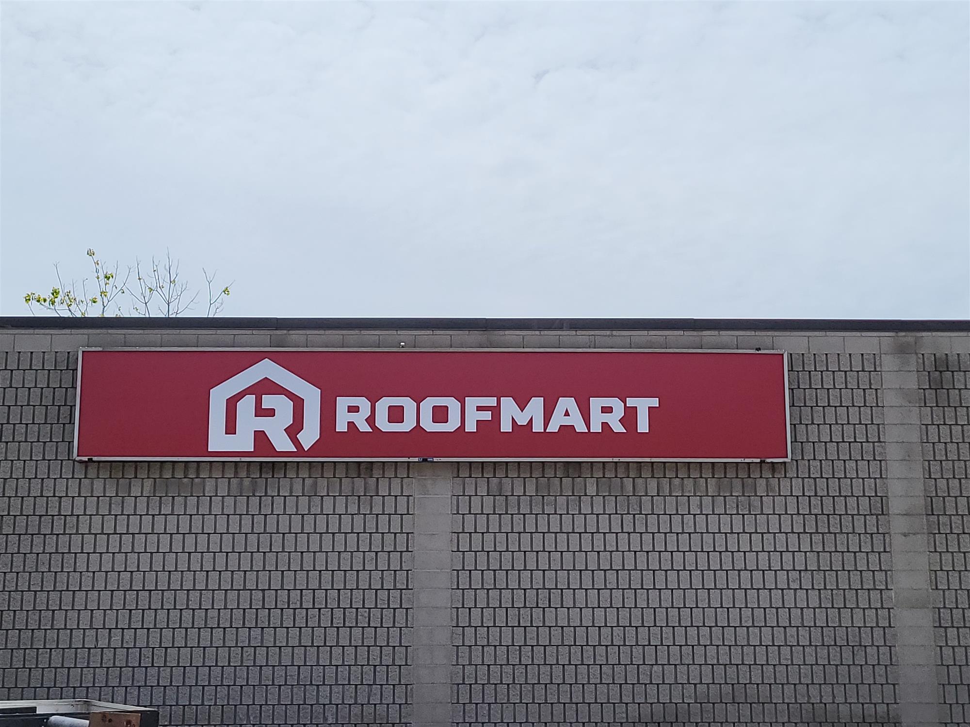 Red and white Roofmart sign on brick building