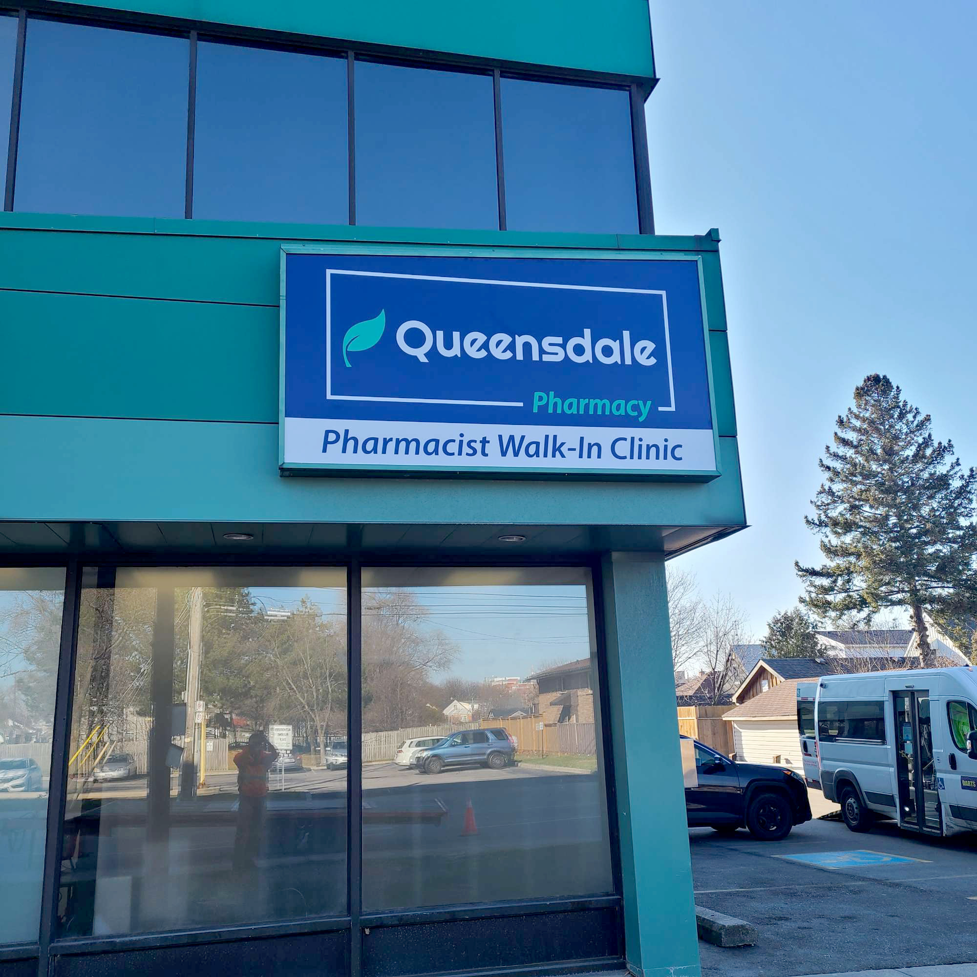 a newly installed blue and green sign on a green building for Queensdale Pharmacy walk in clinic