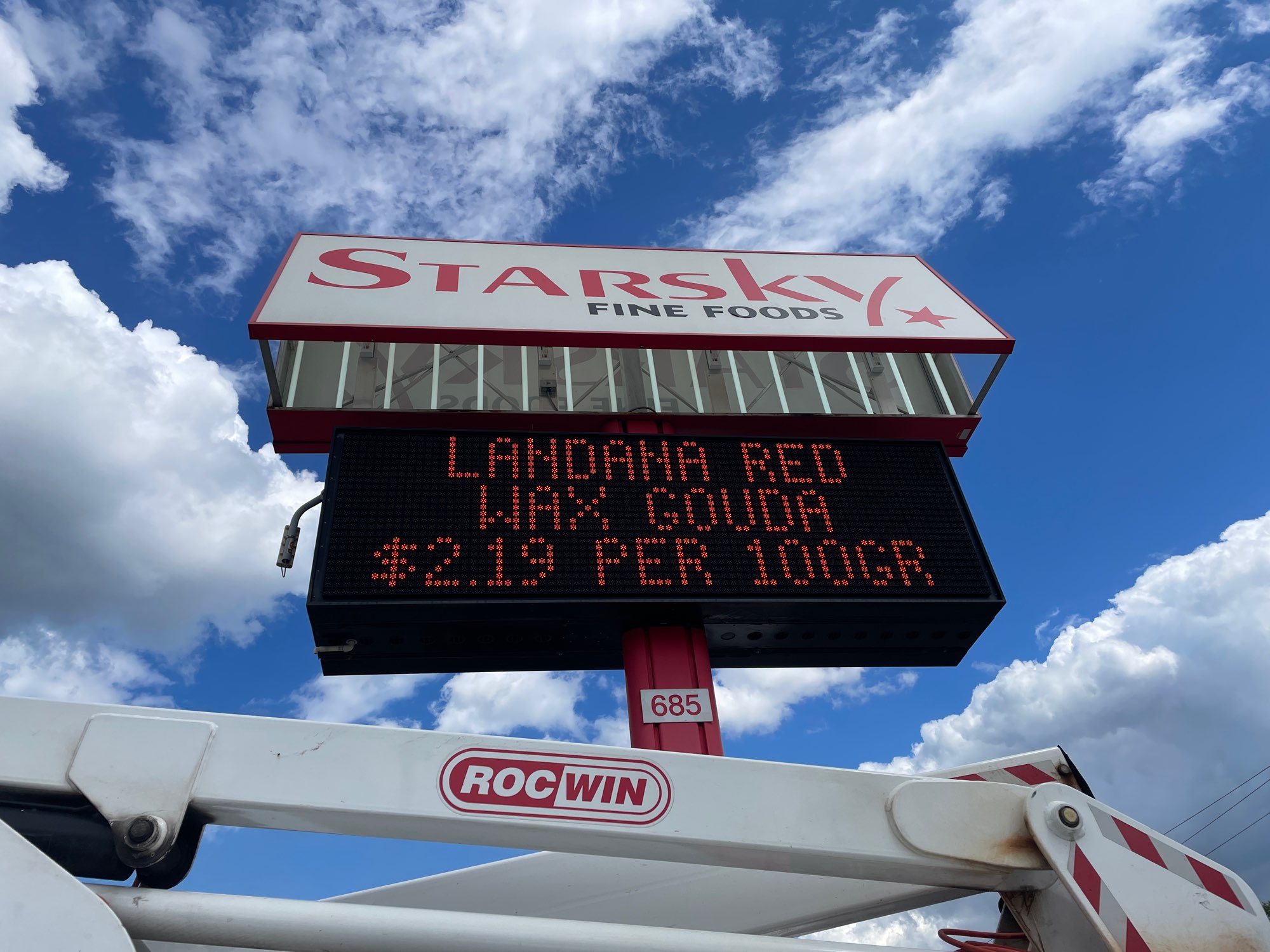 a red and white pylon sign and electronic message centre sign for Starsky Fine Food and a white Yesco truck with blue sky in the background