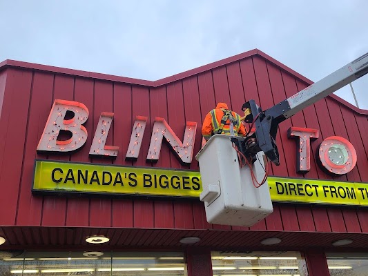 a Yesco technician in an aerial bucket servicing a red and yellow Blinds to Go sign