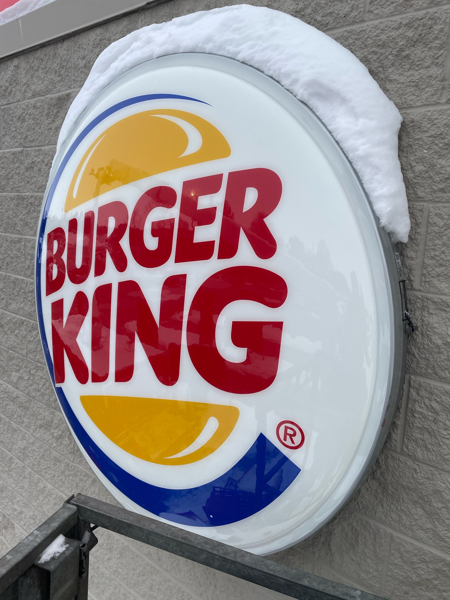 a round red, blue, white and yellow Burger King sign on the side of a brick building