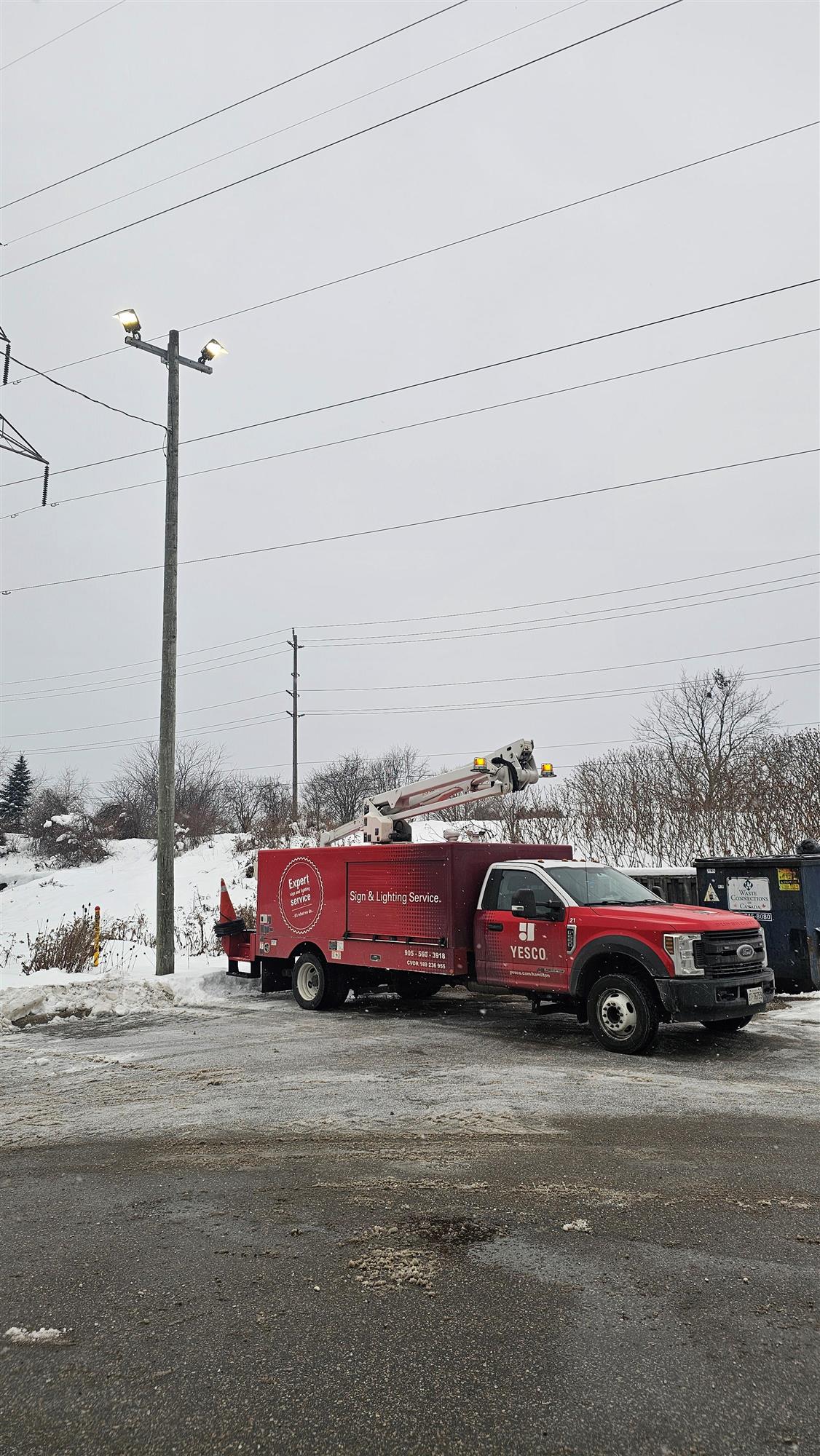 a red Yesco service truck parked beside parking lot light for a replacement
