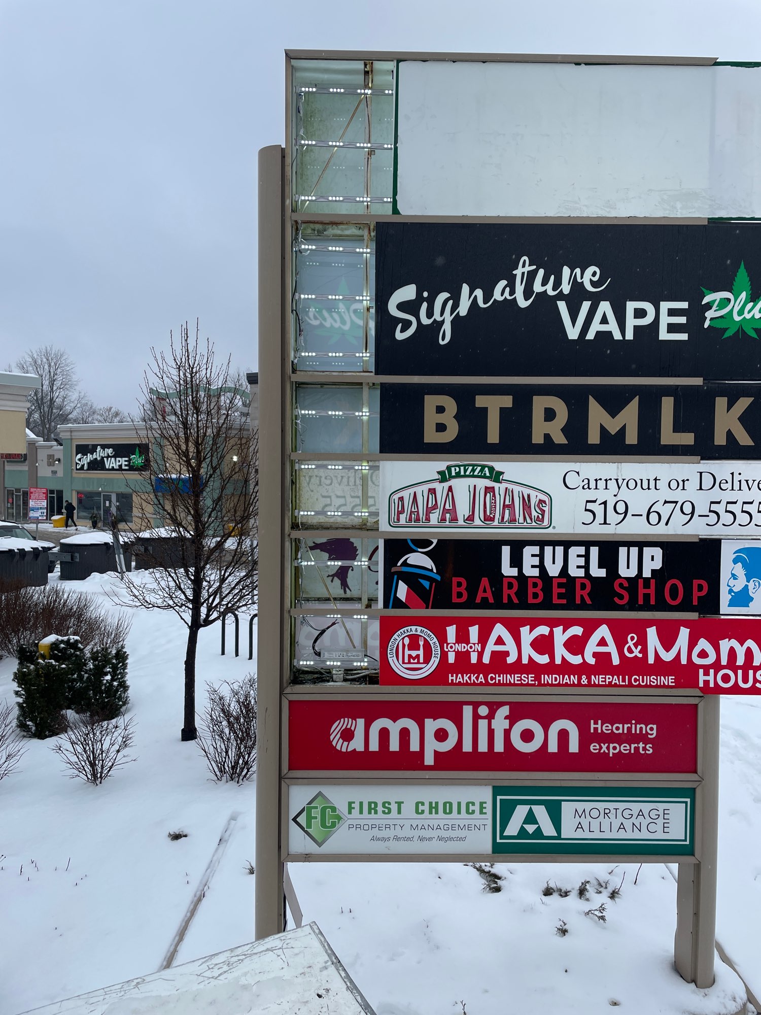 a pylon sign with many businesses list with snow on the ground