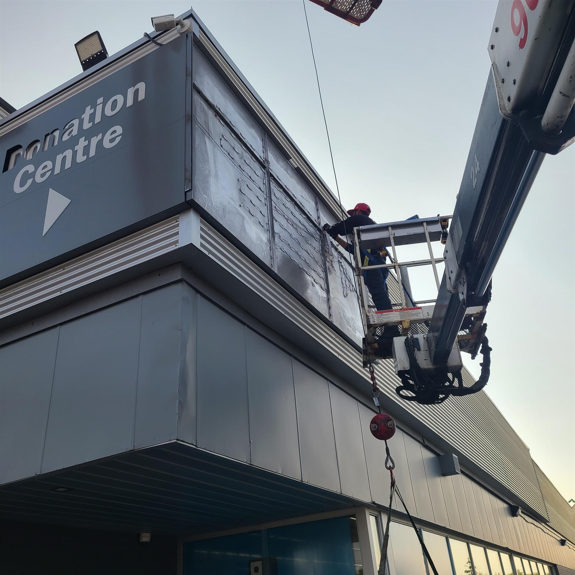 a Yesco sign technician in a large bucket truck repairing the Goodwill sign in Mississauga, Ontario