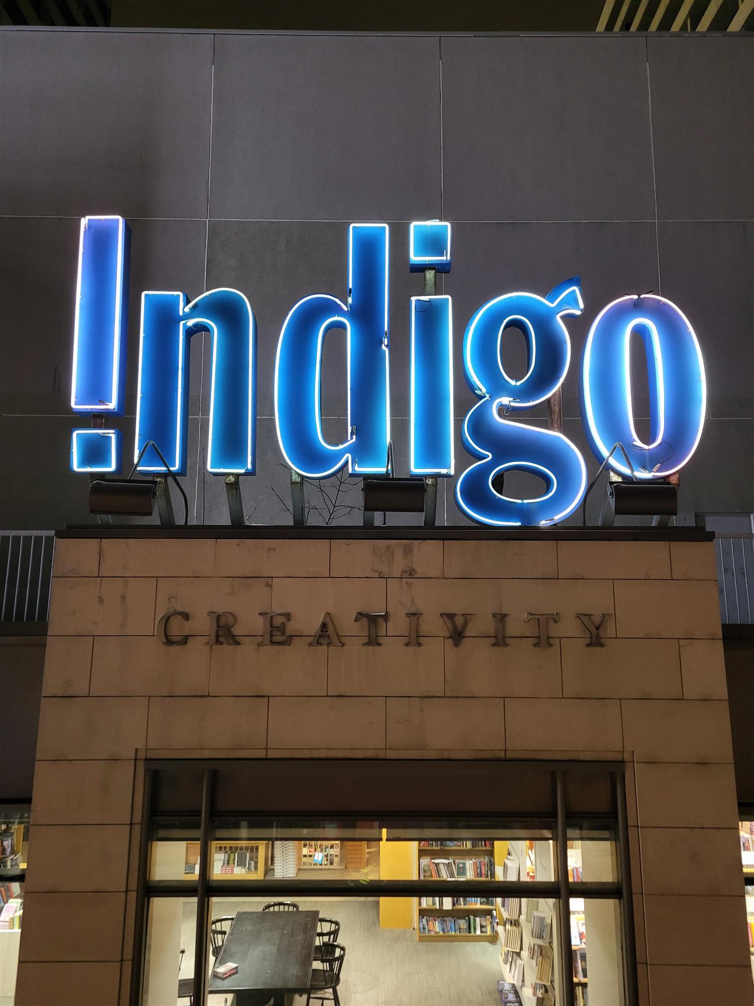 a blue neon sign for Indigo book store above the store entrance