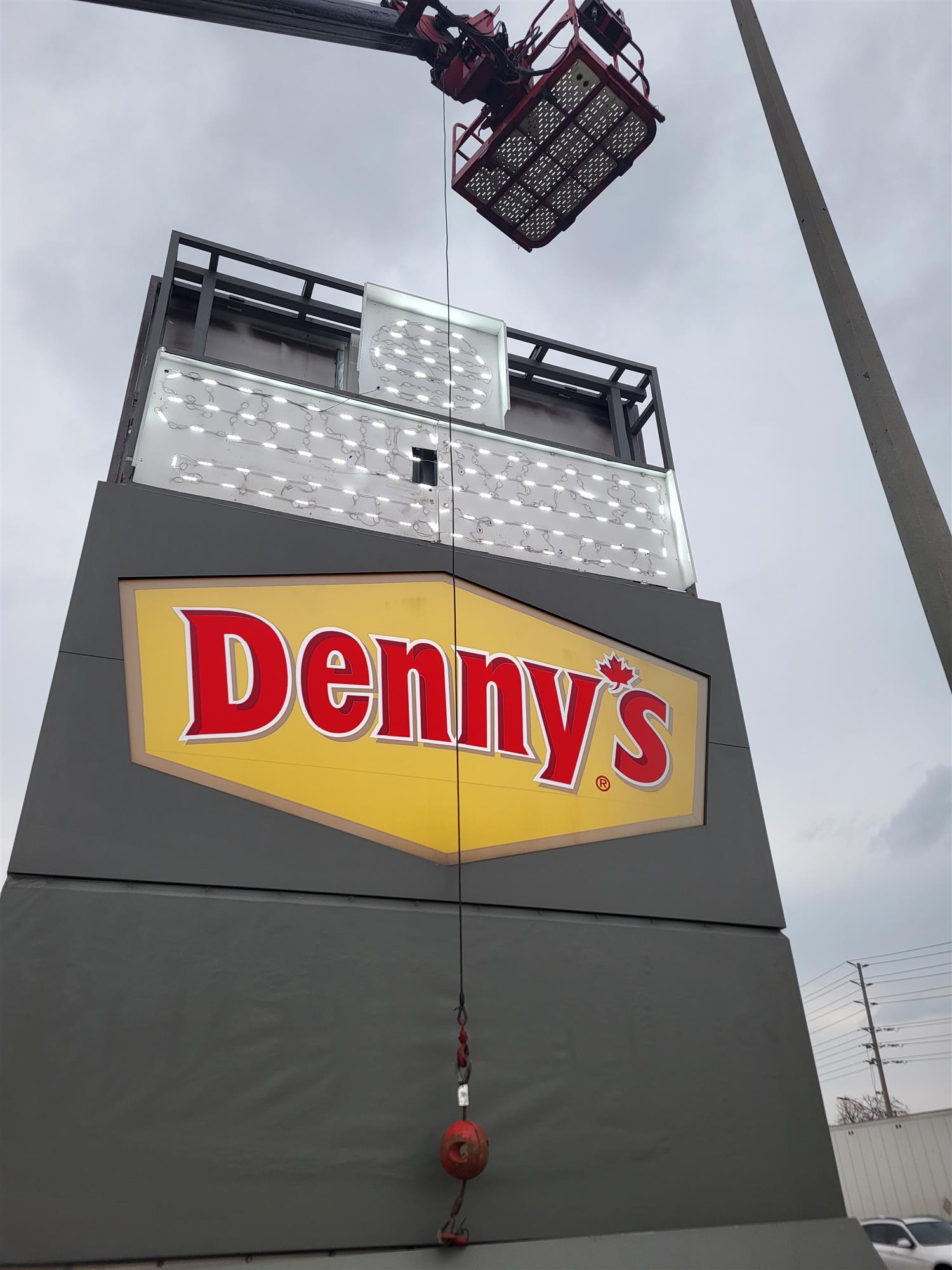 a red and yellow Denny's sign with boom ladder over top for repair