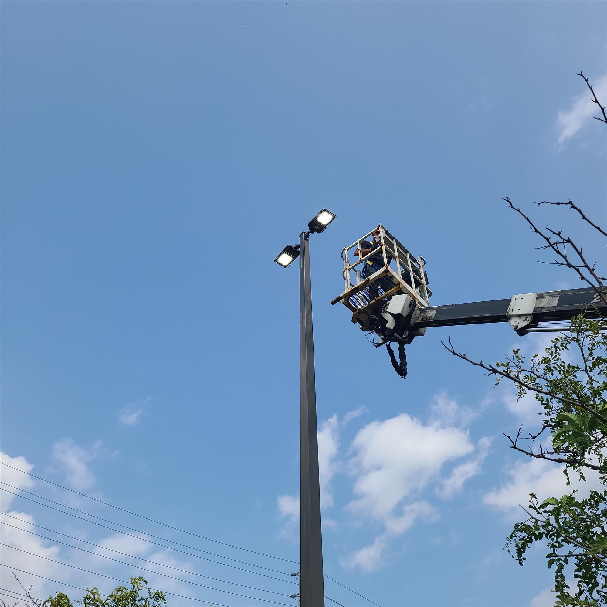 a bucket ladder with a Yesco technician beside a tall pole light a Spark by Hilton hotel