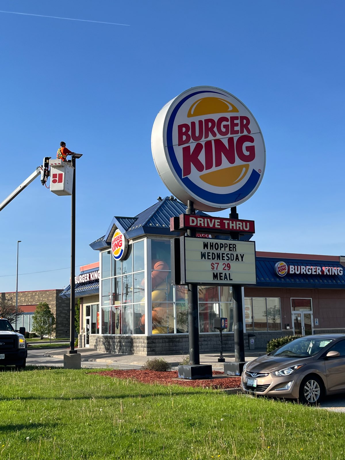 the front of a Burger King restaurant having its parking lot light repaired by a technician in a bucket truck