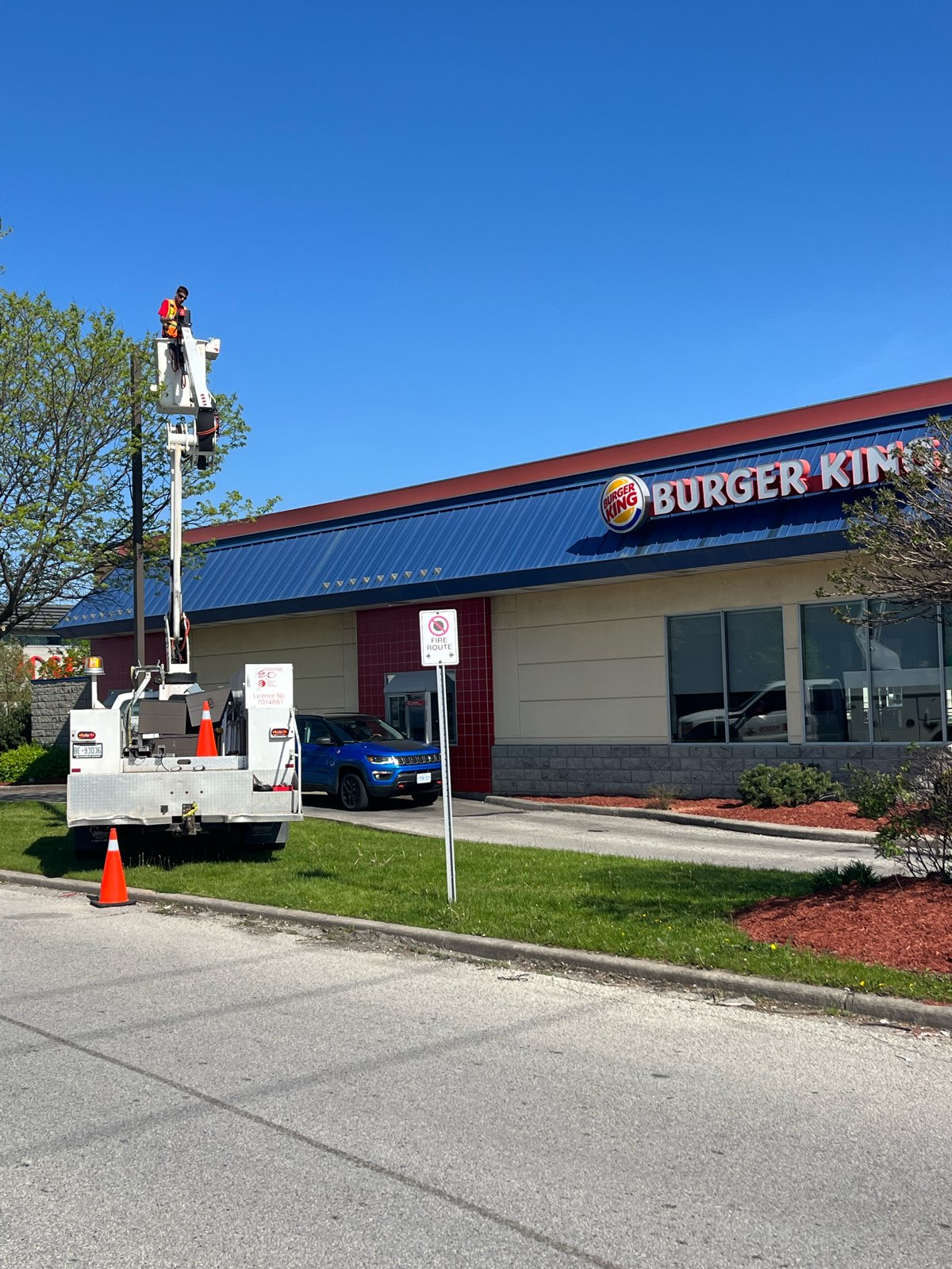 a man in a bucket truck fixing a tall light fixture in front of a burger king restaurant