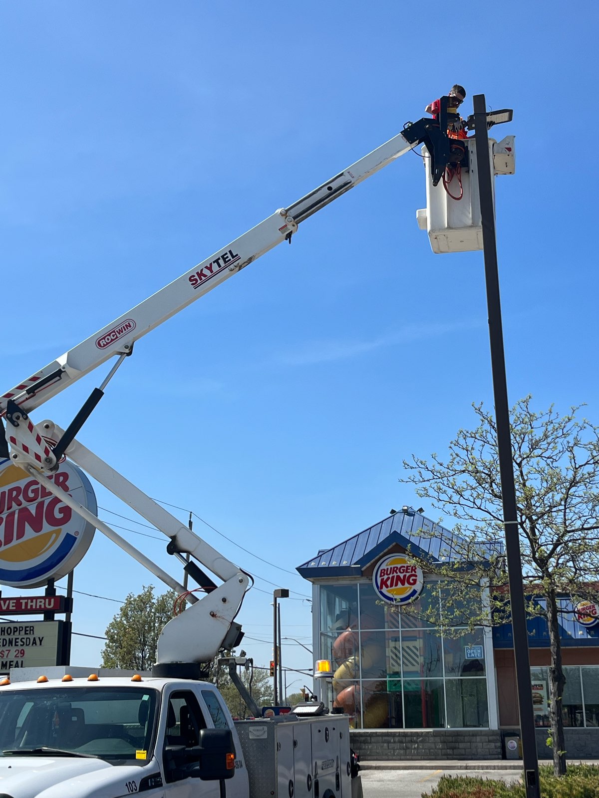 a man in a bucket truck fixing a tall pole parking lot light at a burger king restaurant