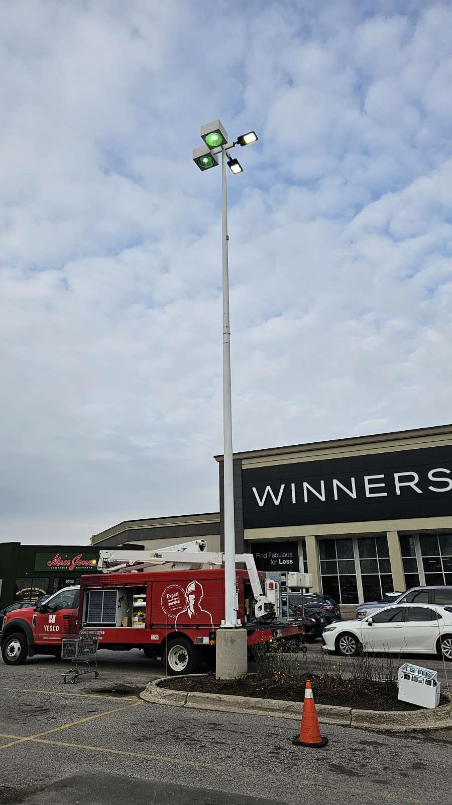 a red yesco truck servicing a large light pole in a Winners parking lot