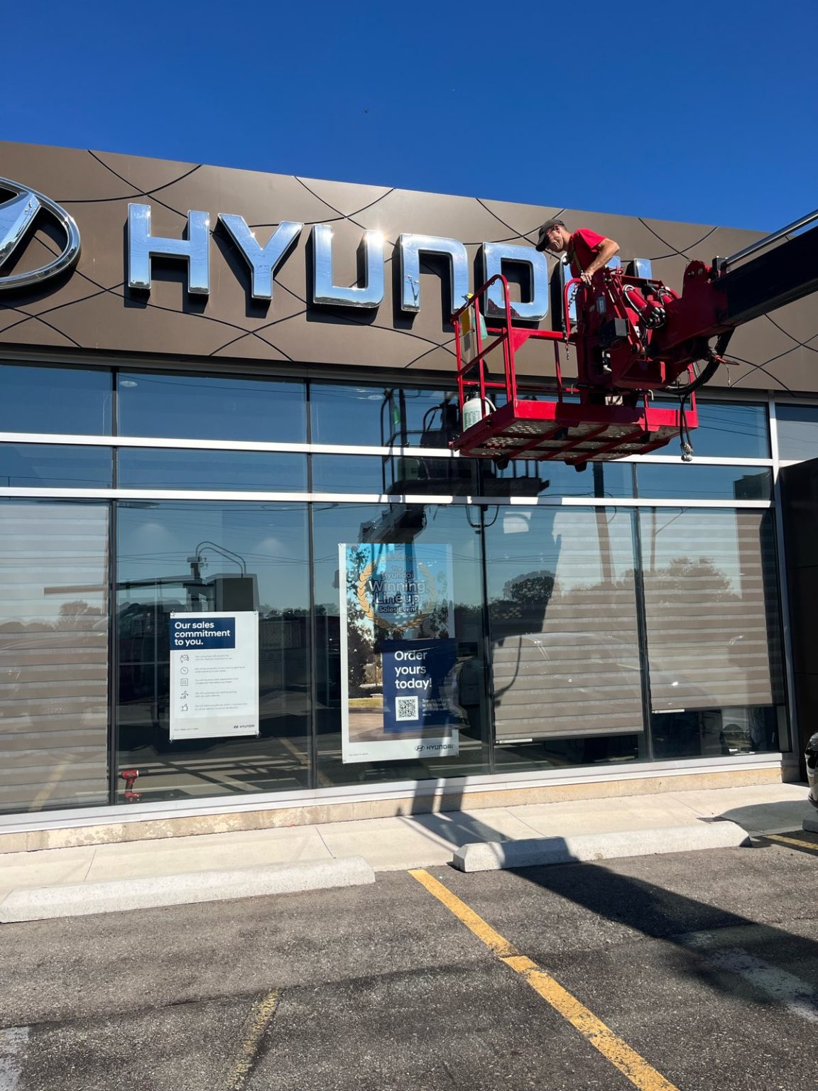 a silver Hyundai sign on the top of the building being repaired by a Yesco technician in a large bucket