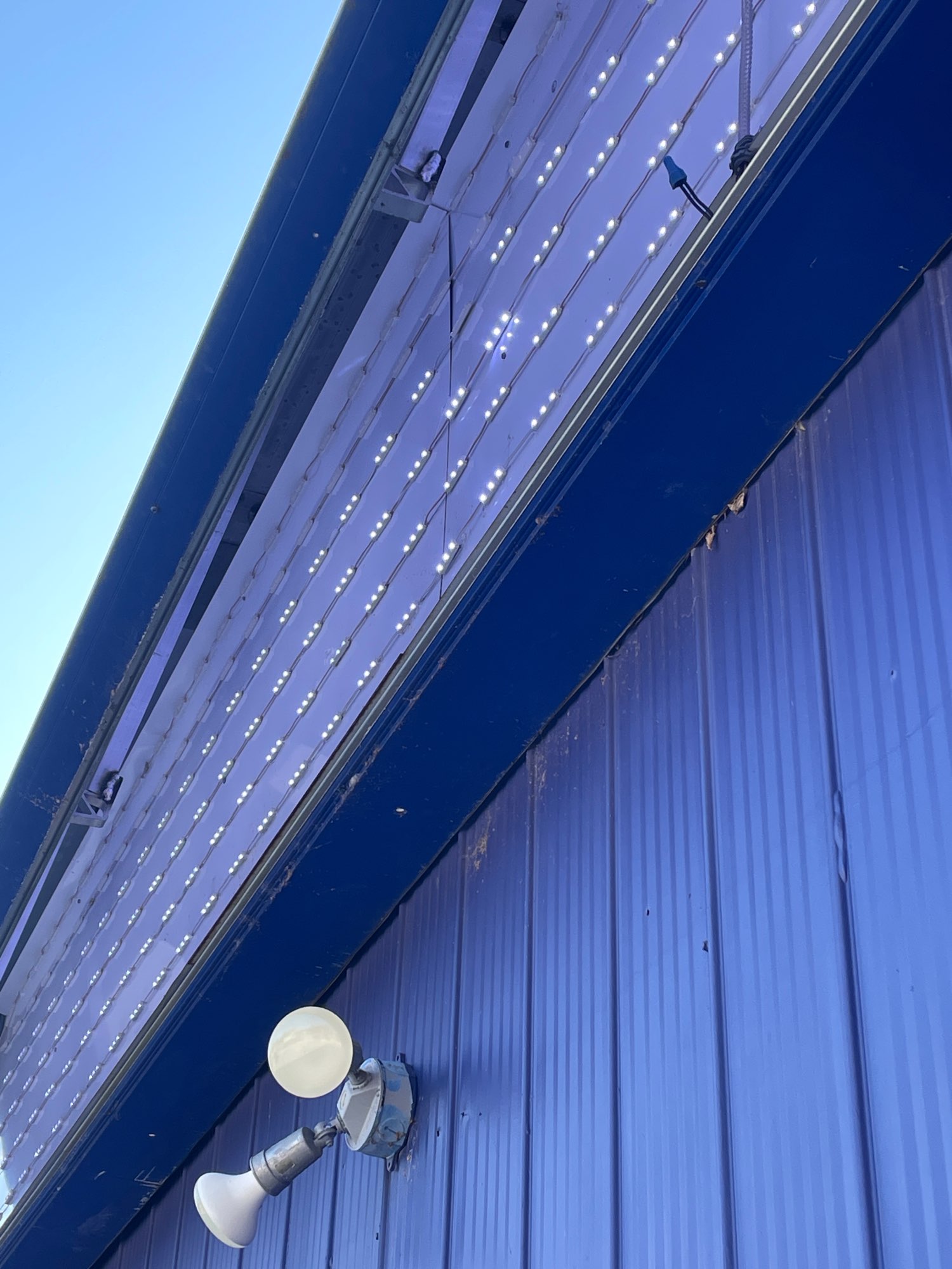 the side of a blue building showing LED lights from the inside of a sign that is being repaired