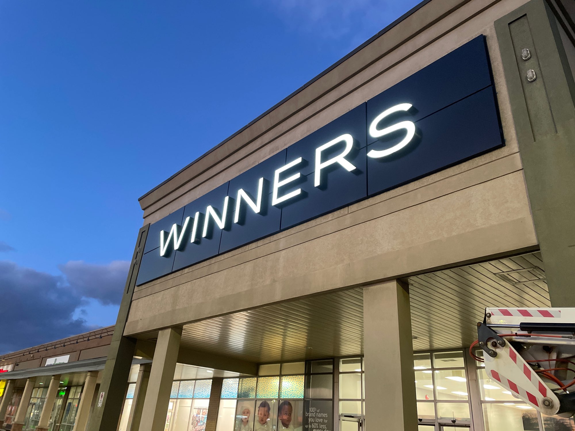 in the evening in front of a Winners store with the letters of the sign illuminated