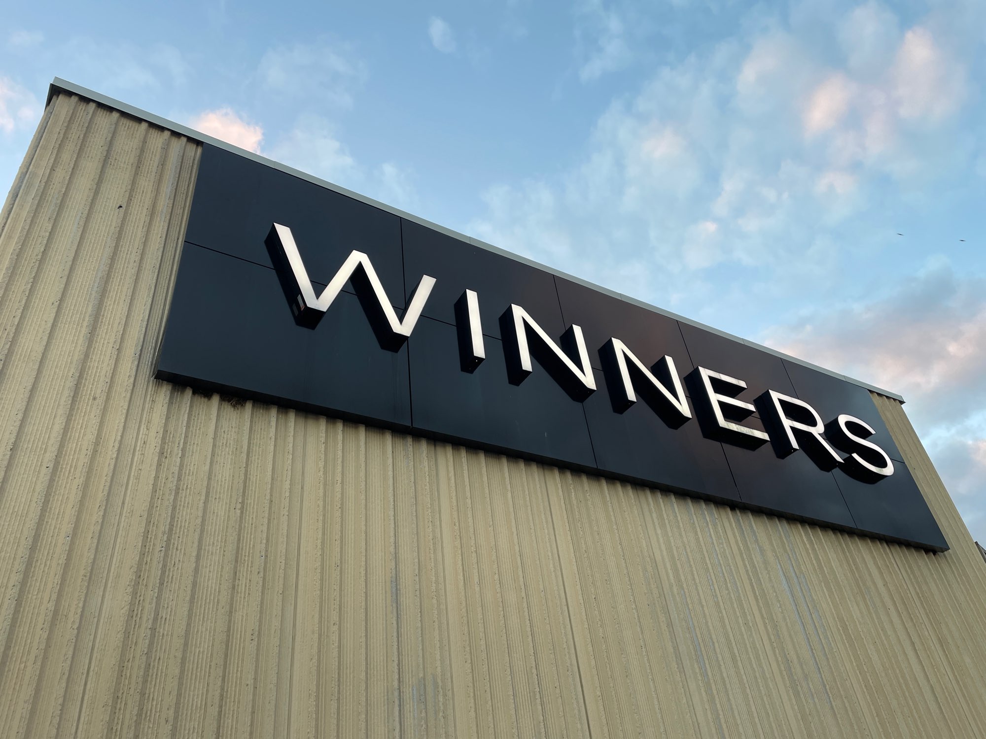 a black and white winners sign on the side of store with blue sky above