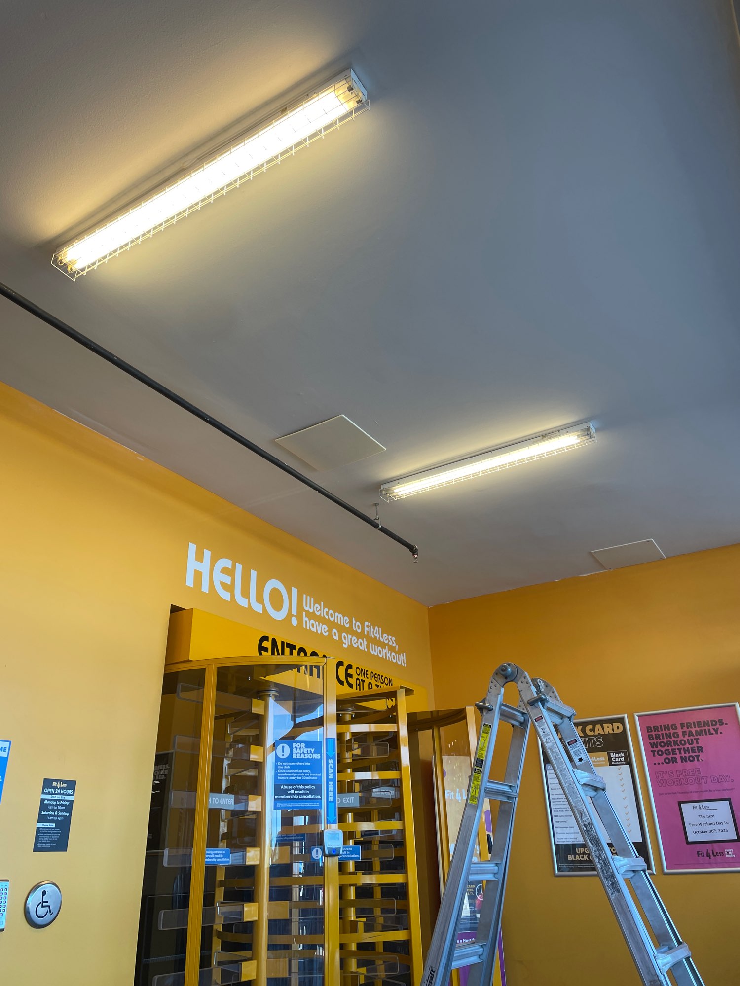 bright overhead lights inside the fit4less gym with bring yellow walls